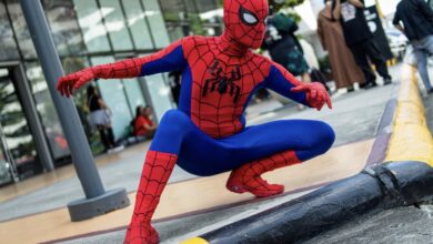 Cosplayer Cyan Blur crouches in a red-and-blue Spider-Man costume beside a curb.