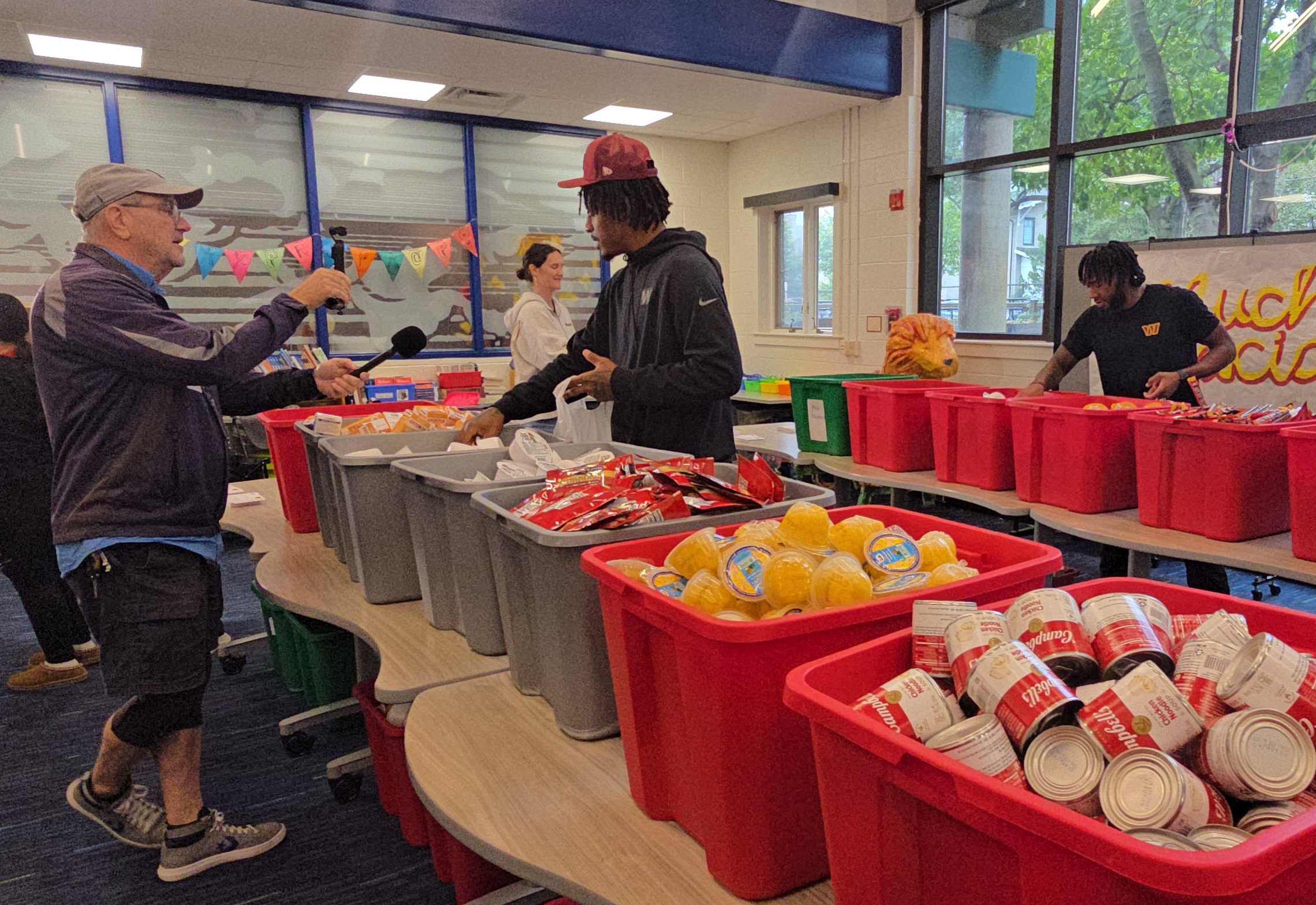 Rasul Douglas and Jaylin Lane Pack Food Bags Washington Commanders cornerback Rasul Douglas, wearing a burgundy cap, and wide receiver Jaylin Lane pack food bags among bins of canned goods at Mount Vernon Community School.