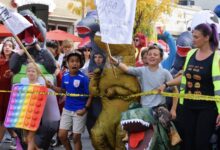 Children and adults in dinosaur and rainbow pop-it costumes at the 2023 Del Ray Halloween Parade.