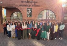 Ribbon-cutting attendees hold a red ribbon outside Wonderologie Counseling + Wellness on Mount Vernon Avenue.