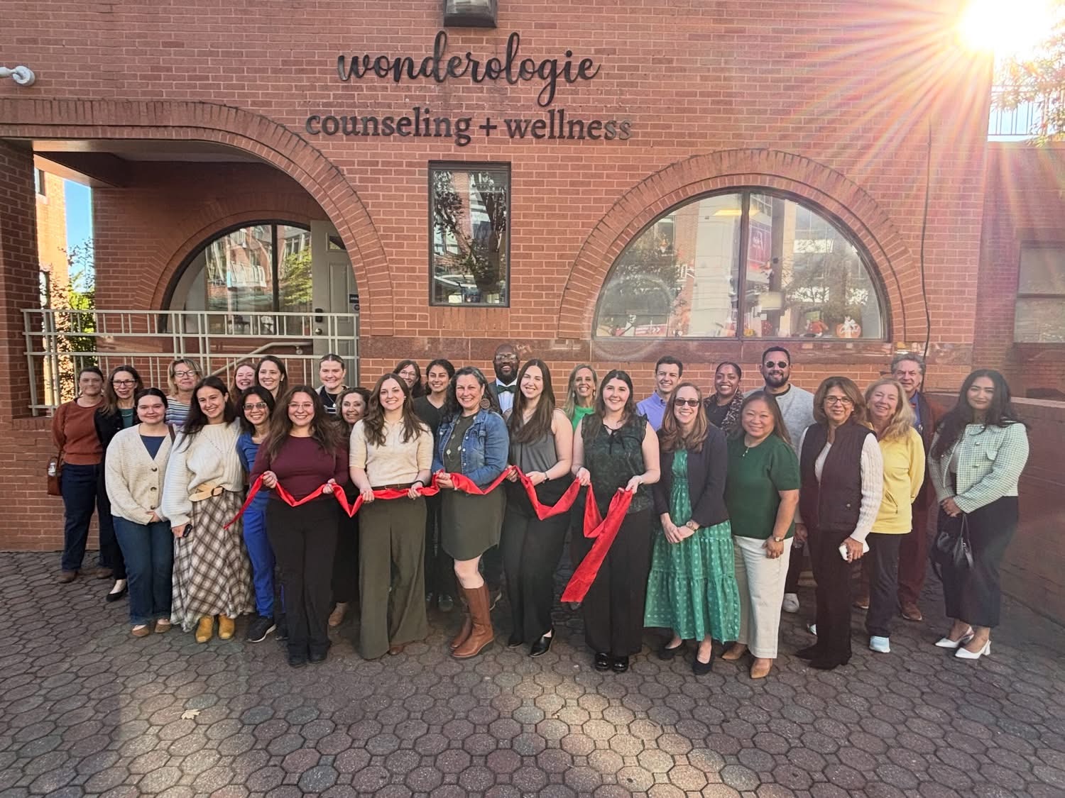 Ribbon-cutting attendees hold a red ribbon outside Wonderologie Counseling + Wellness on Mount Vernon Avenue.