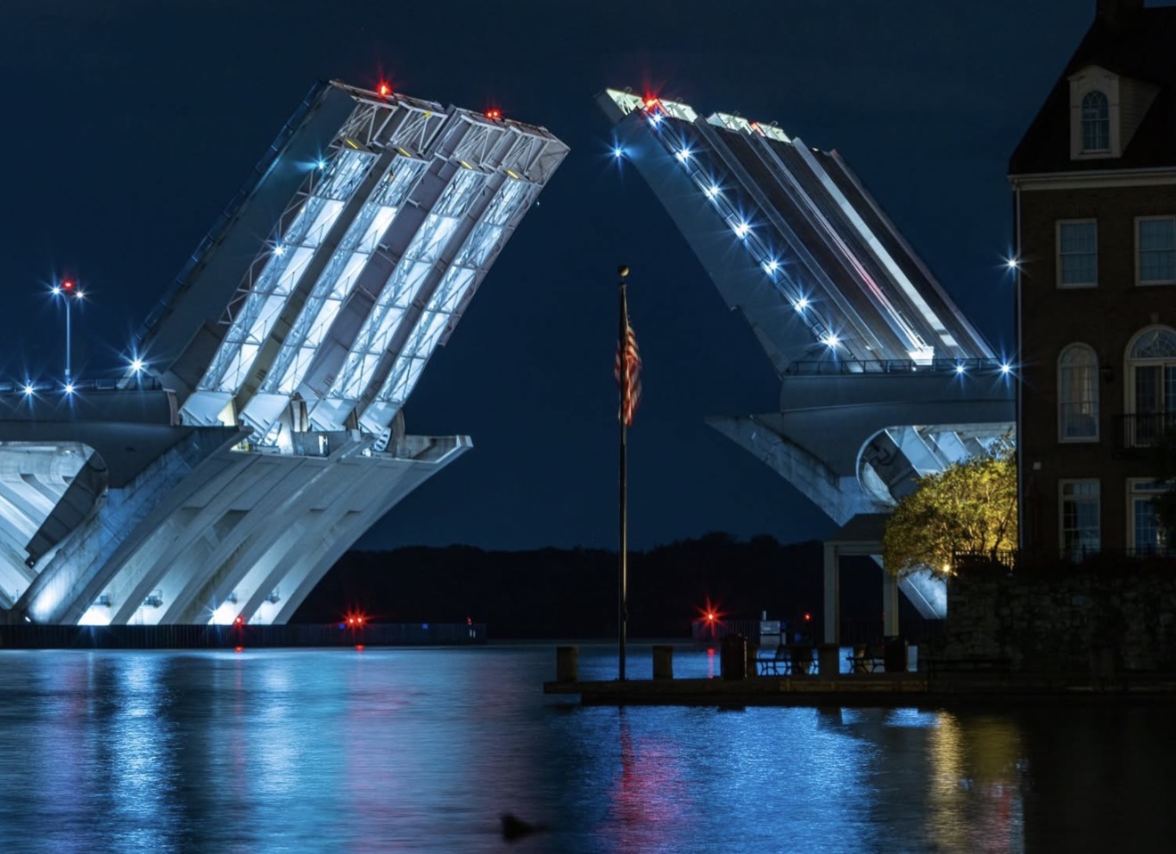 The illuminated Woodrow Wilson Bridge with both drawbridge spans raised at night over the Potomac River.