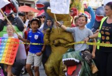 Children in dinosaur and rainbow pop-it costumes join participants at the 2023 Del Ray Halloween Parade.