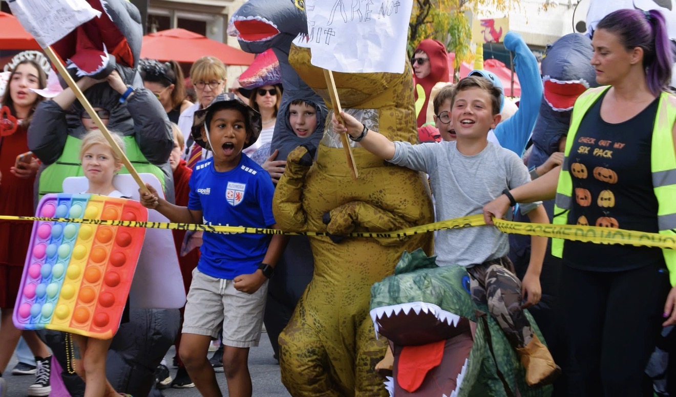 Children in dinosaur and rainbow pop-it costumes join participants at the 2023 Del Ray Halloween Parade.