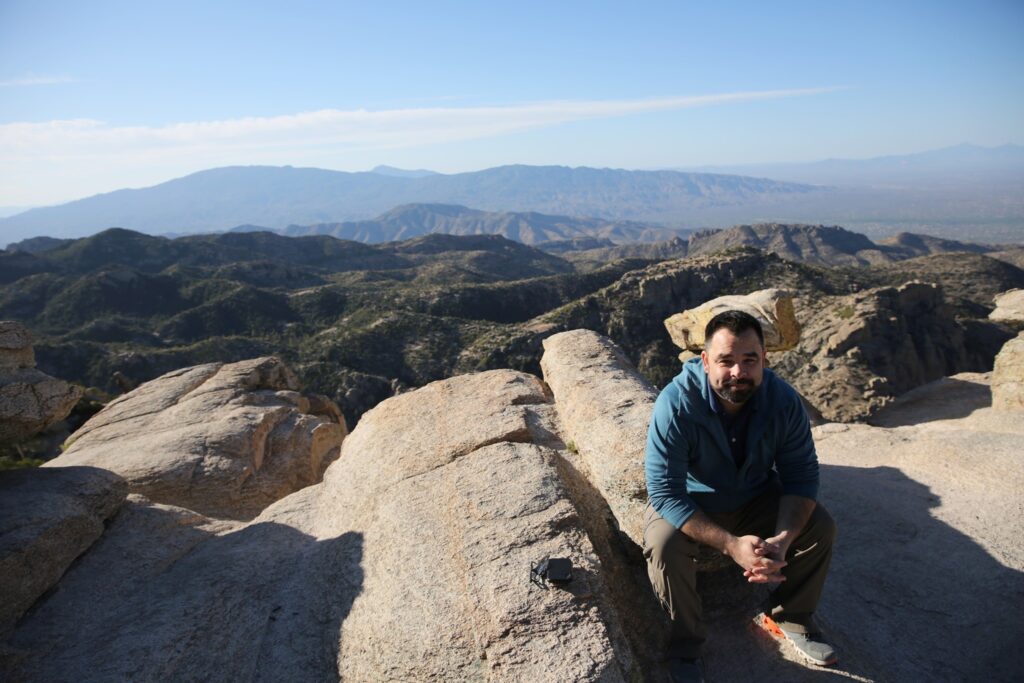 Jimmy Epp, who offers communication skills training, sits on top of a mountain outside of Arizona.