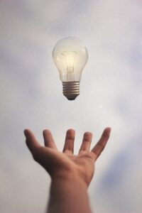 person's hand with light bulb floating above it