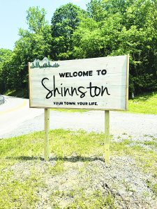 photo of "Welcome to Shinnston" sign with trees and road in background