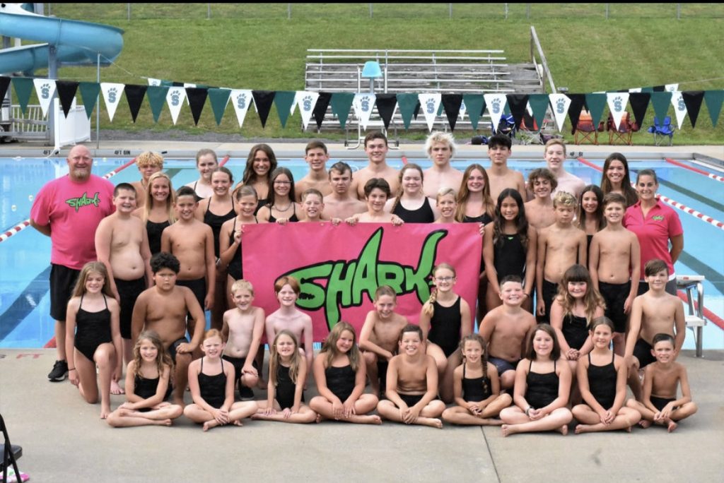 team photo by pool with pink and green sharks sign