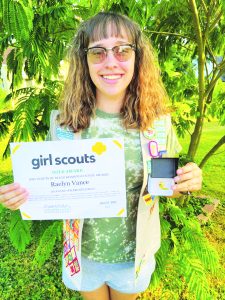 Raelyn holding certificate, smiling, greenery behind her