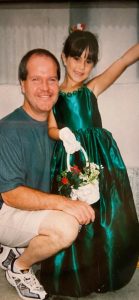 Marissa in a green dress, arm up as if it to say "look at me" with flowers, both smiling