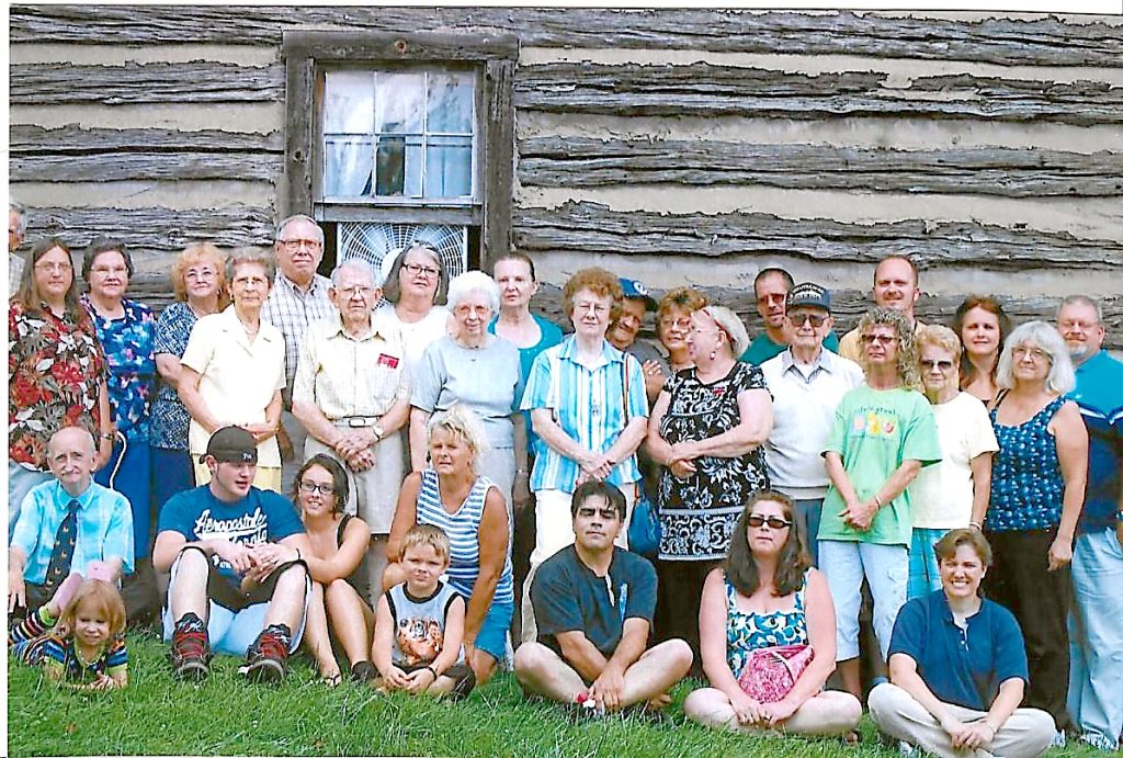 group is standing in front of a log cabin. About 30 people.