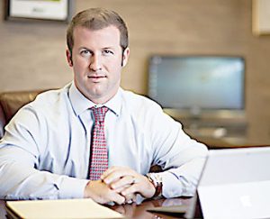 Trey in dress shirt and red tie, at desk