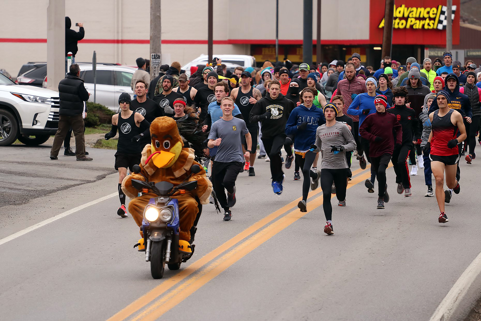 large group, some in cold-weather clothing and some in tank tops and shorts, runs on Pike Street behind the moped