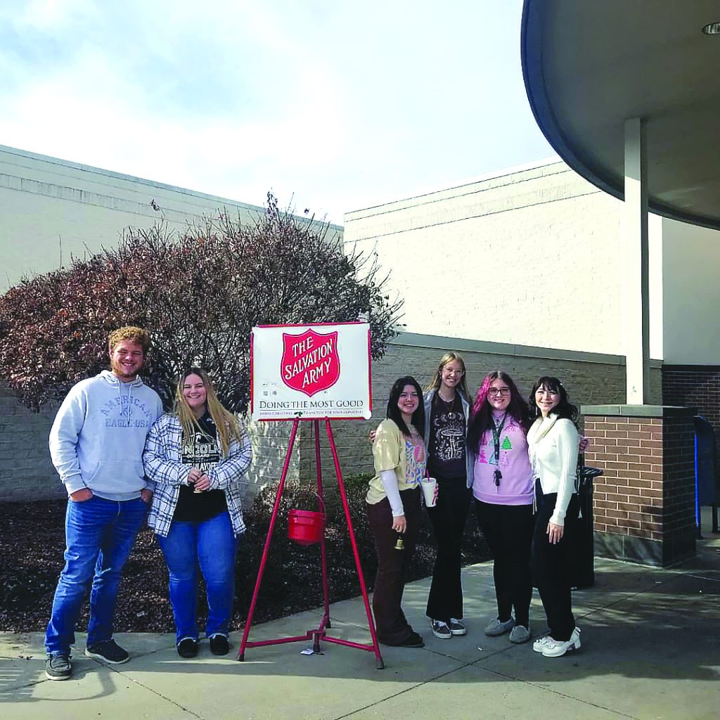 Bell-ringers  stand with the Salvation Army sign and red kettle.