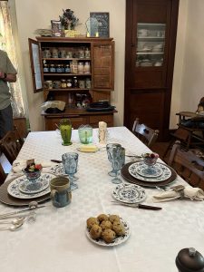 table is made with china plates, blue drinking glasses, a plate of muffins, on a white tablecloth