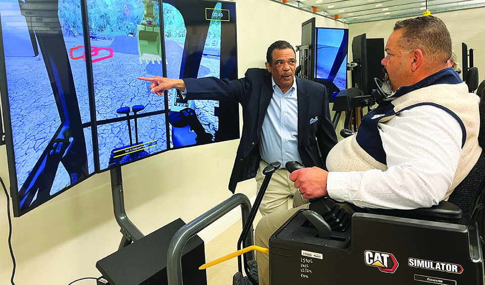 HEO Instructor Michael Scales demonstrates excavator operation on a CAT simulator for Patrick County Director of Economic Development and Tourism James Houchins.