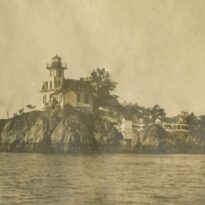 Sepia photo of a lighthouse taken from the water.