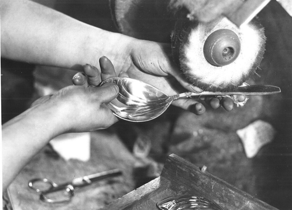 Black and white photograph of a silver spoon being polished at the Gorham Manufacturing Company, from the RIHS collection, not featured in the article.