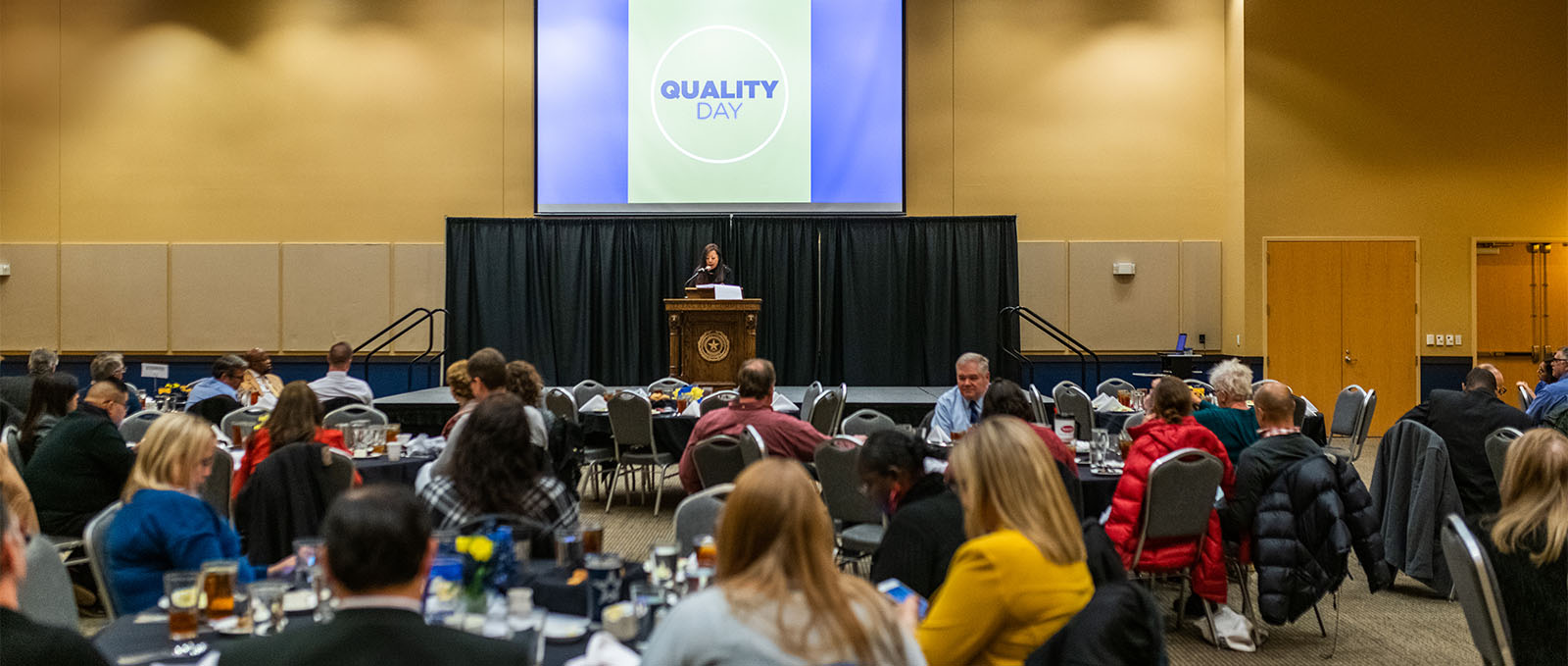 Speaker talking to audience sitting at round tables during a conference.