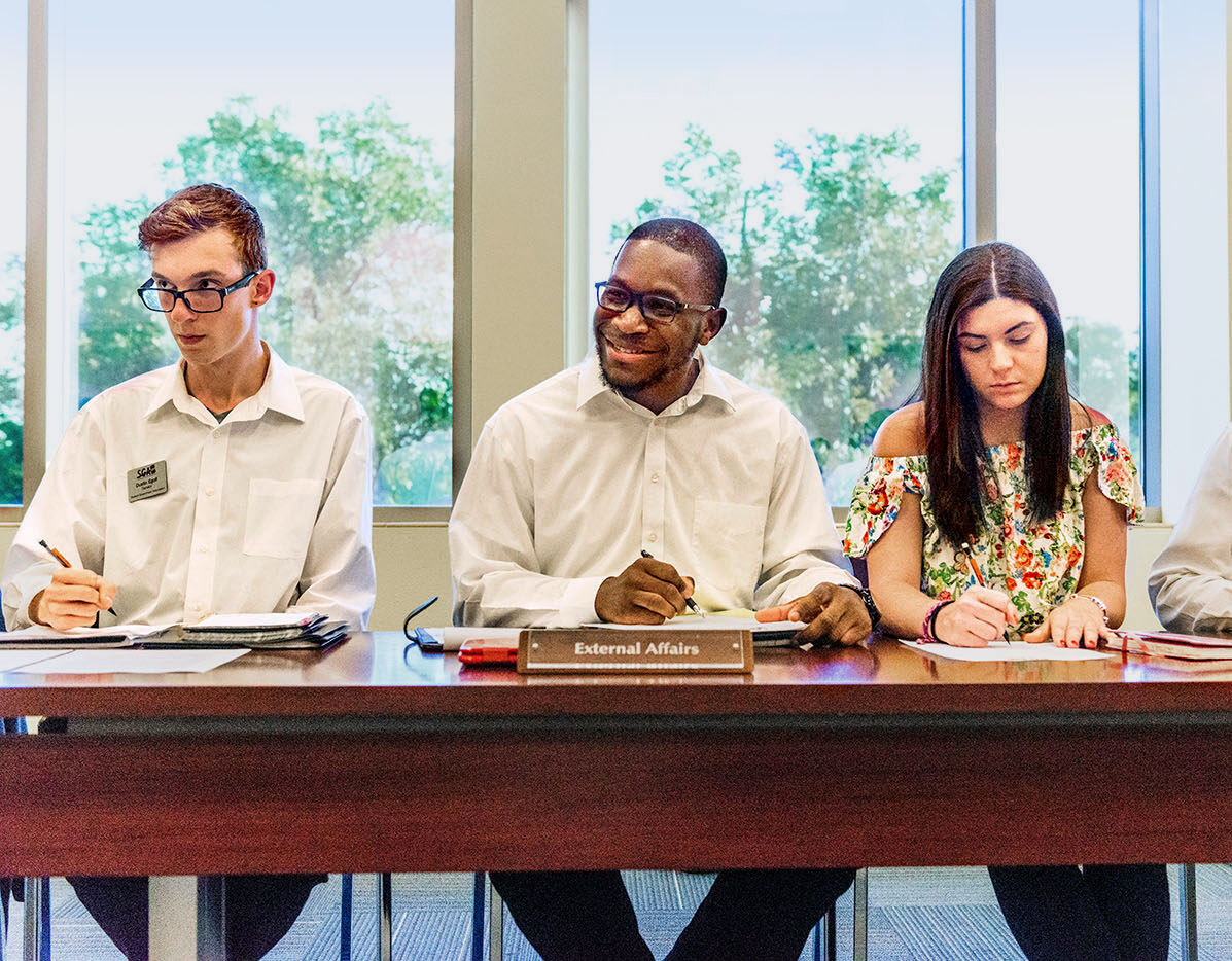 Three student siting at a desk during a SGA meeting.