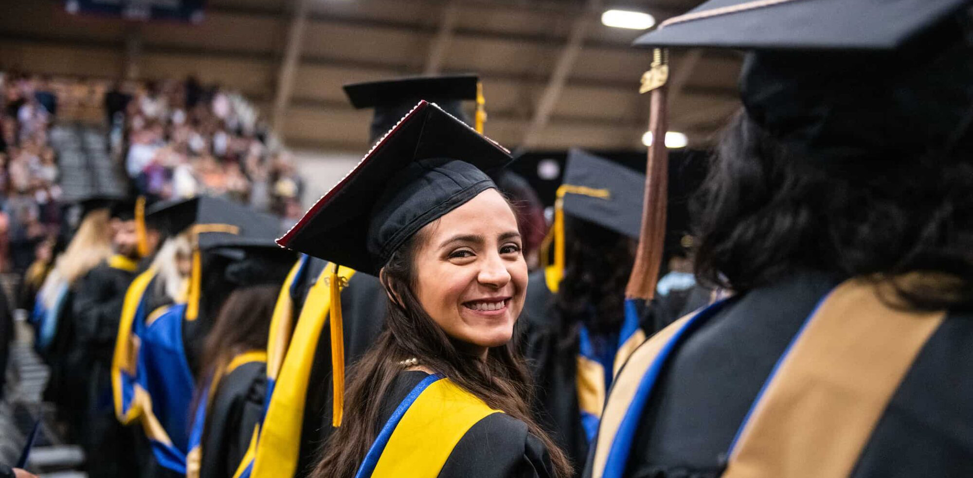 student smiling wearing cap and gown during the graduation ceremony.