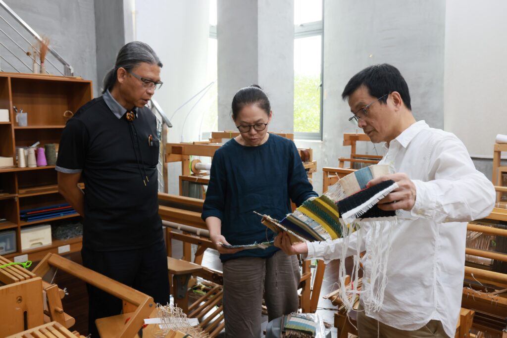 臺南藝術大學材質創作與設計系教授陸佳暉（中）說明該系纖維工作室教學場域及學生作品，右為系主任鄭正雄，左為工藝中心主任陳殿禮。（圖/工藝中心提供）