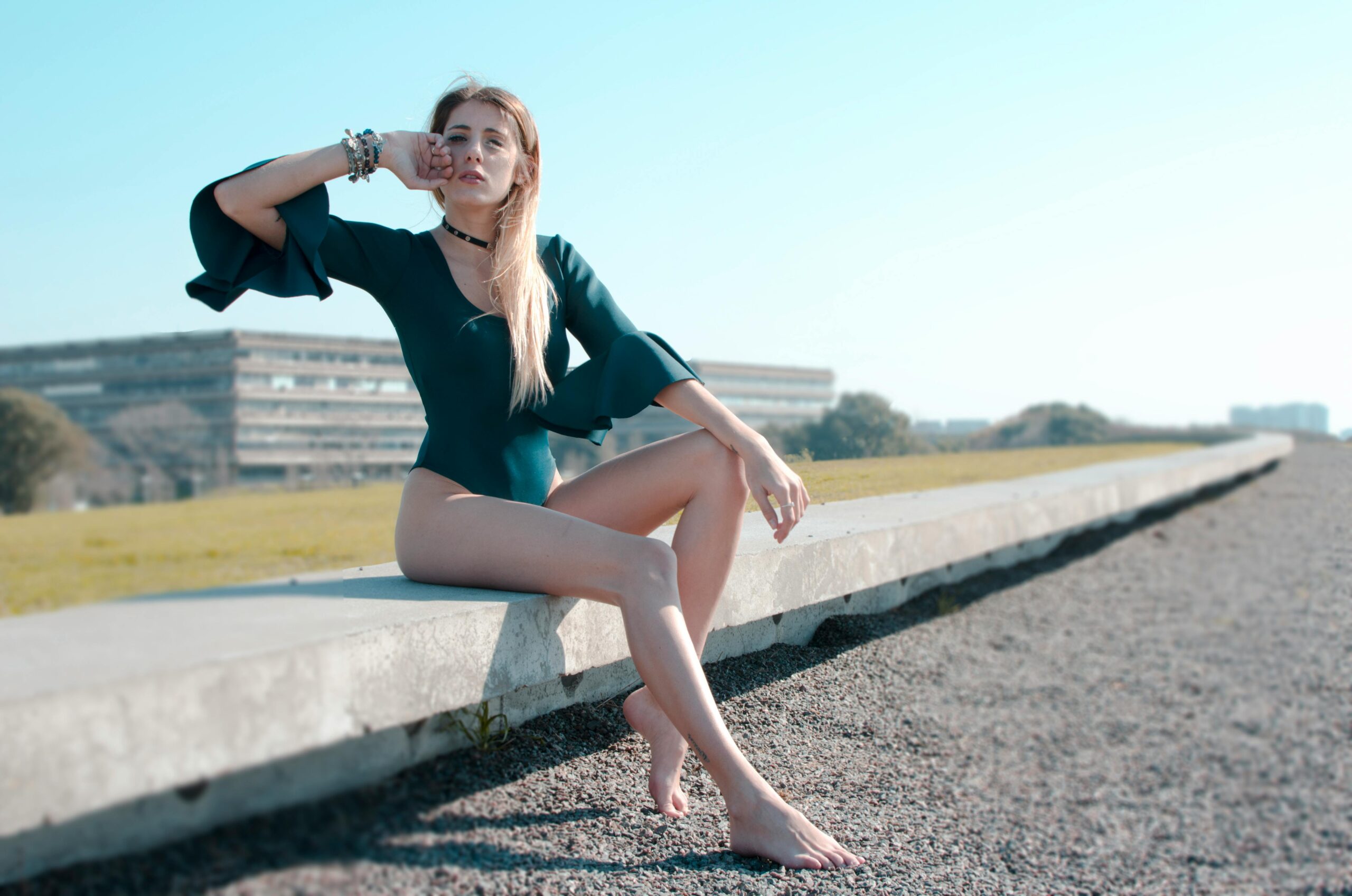 a woman sat on wall with her hand over her eyes wearing a black bodysuit