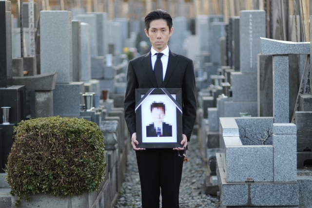 遺影を持つ喪服男性