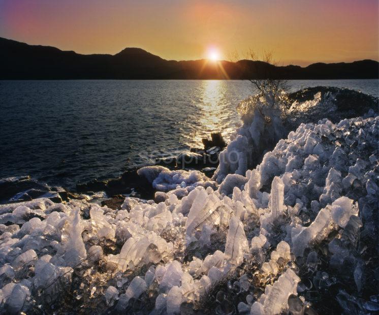 ICE ON ROCKY SHORE OF LOCH ASSYNT AT SUNSET