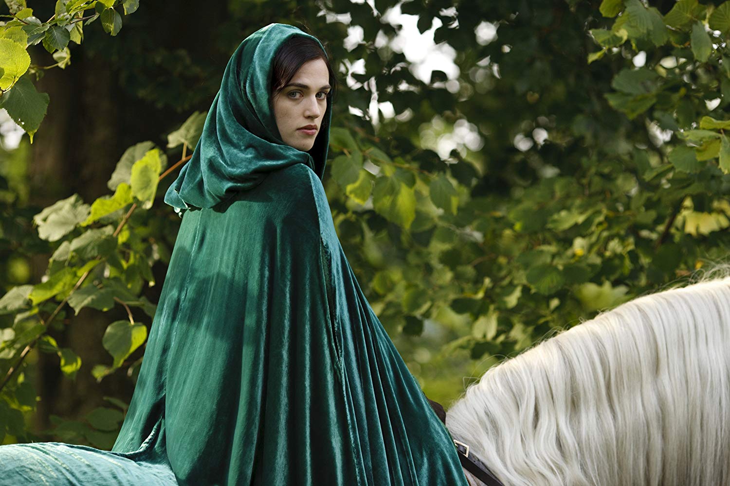 She wears a green cloak and rides a horse.