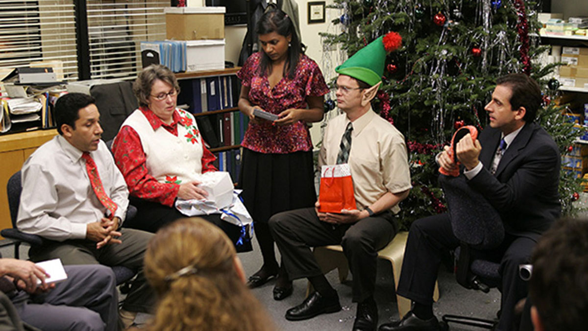 Michael, Dwight, Kelly, Phyllis, and Oscar sit in a circle at a Christmas Party in sitcom, The Office.