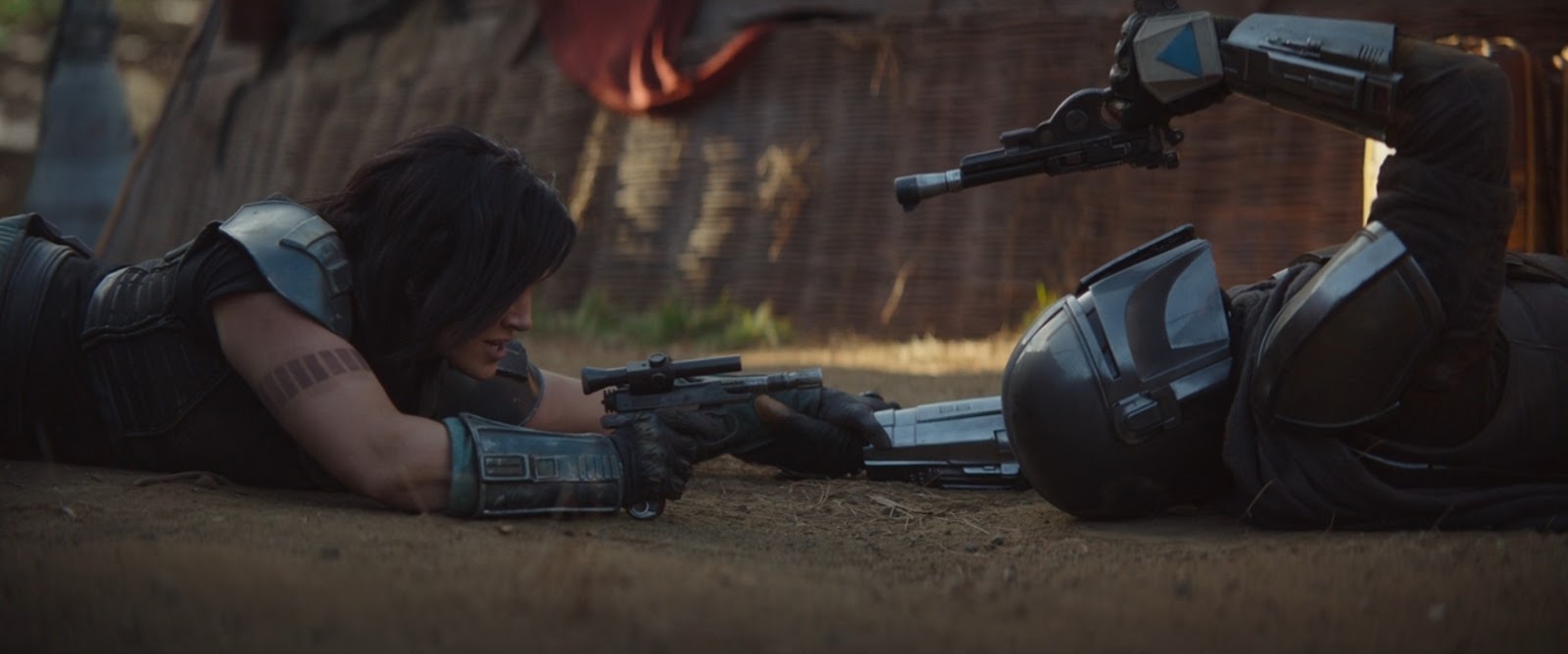 Mando (Pedro Pascal) and Cara Dune (Gina Carano) pointing guns at each other on the ground.