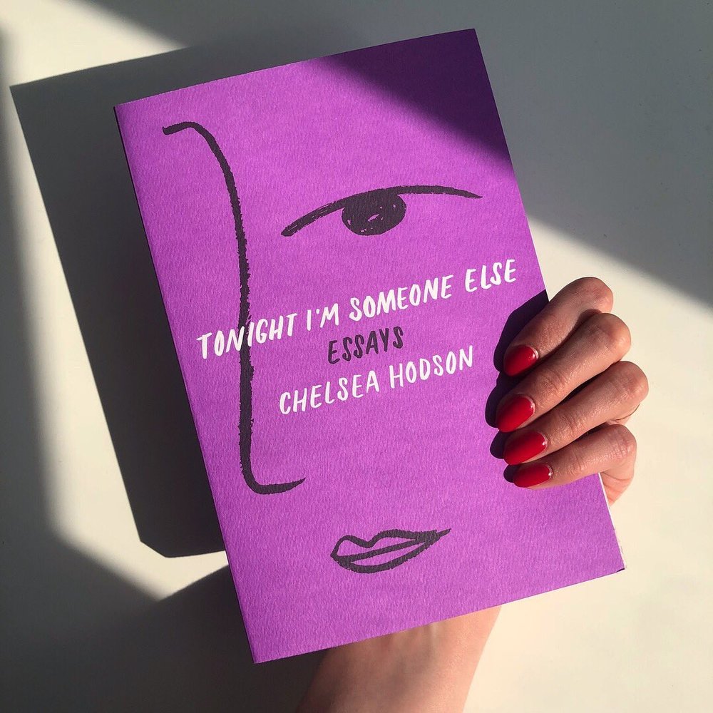 Chelsea Hodson's arm holding the book Tonight I'm Someone Else in front of a white wall.