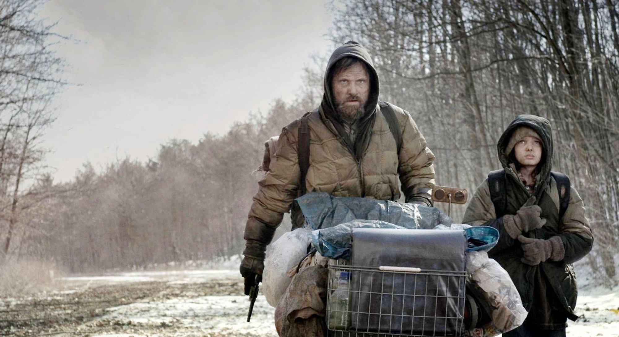 A man and his son, walking down a road with a shopping cart that is filled with what they need to survive in a post-apocalyptic world.