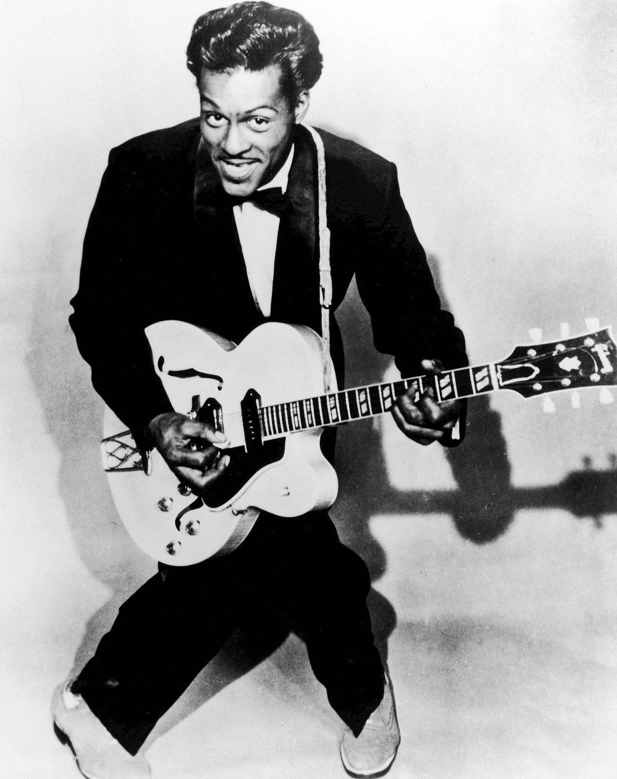 Chuck Berry posing in a tuxedo with his epiphone guitar in black-and-white.