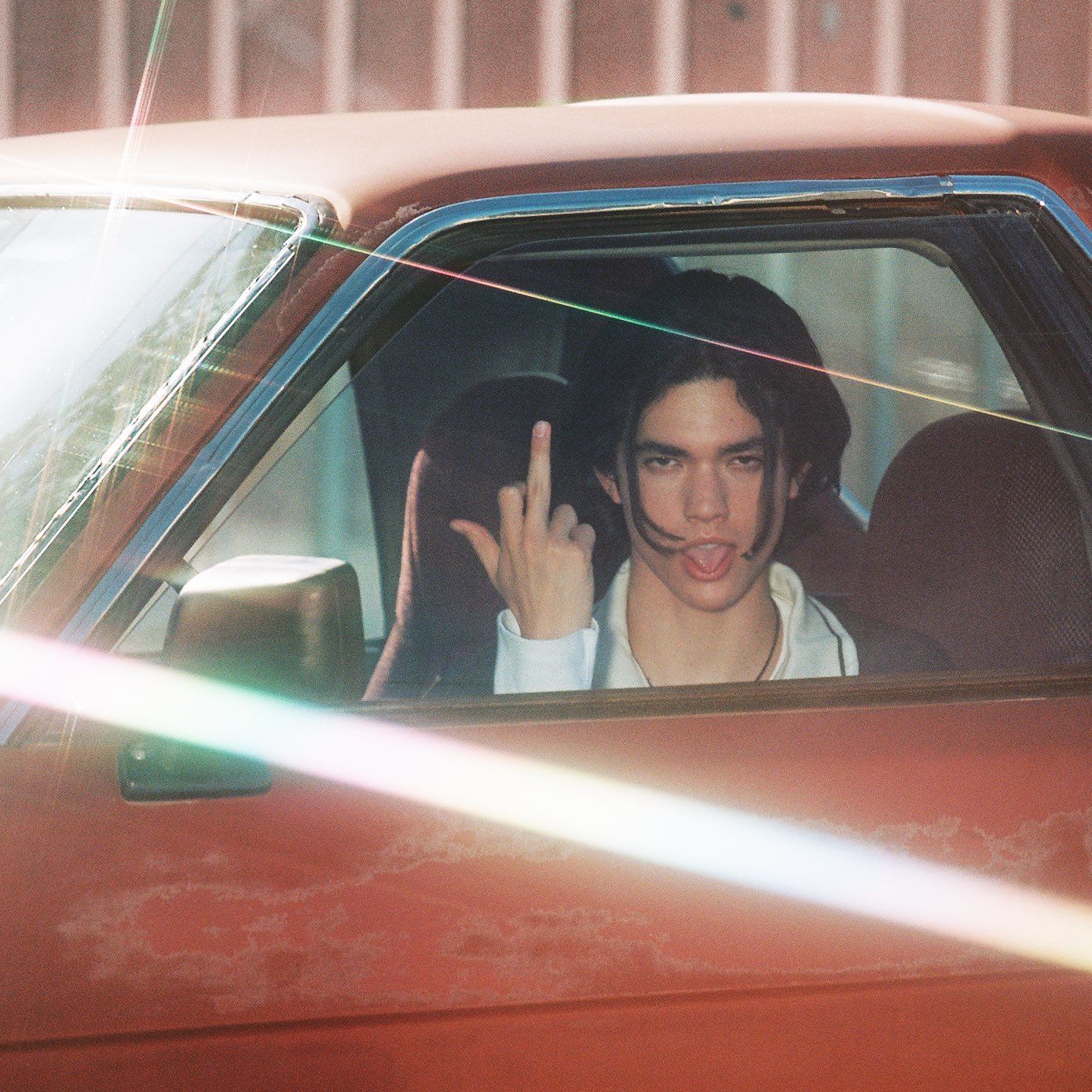 Conan Gray sitting in red car with middle finger up 