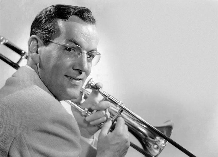 Glenn Miller smirks over his shoulder as he poses with his trombone. 