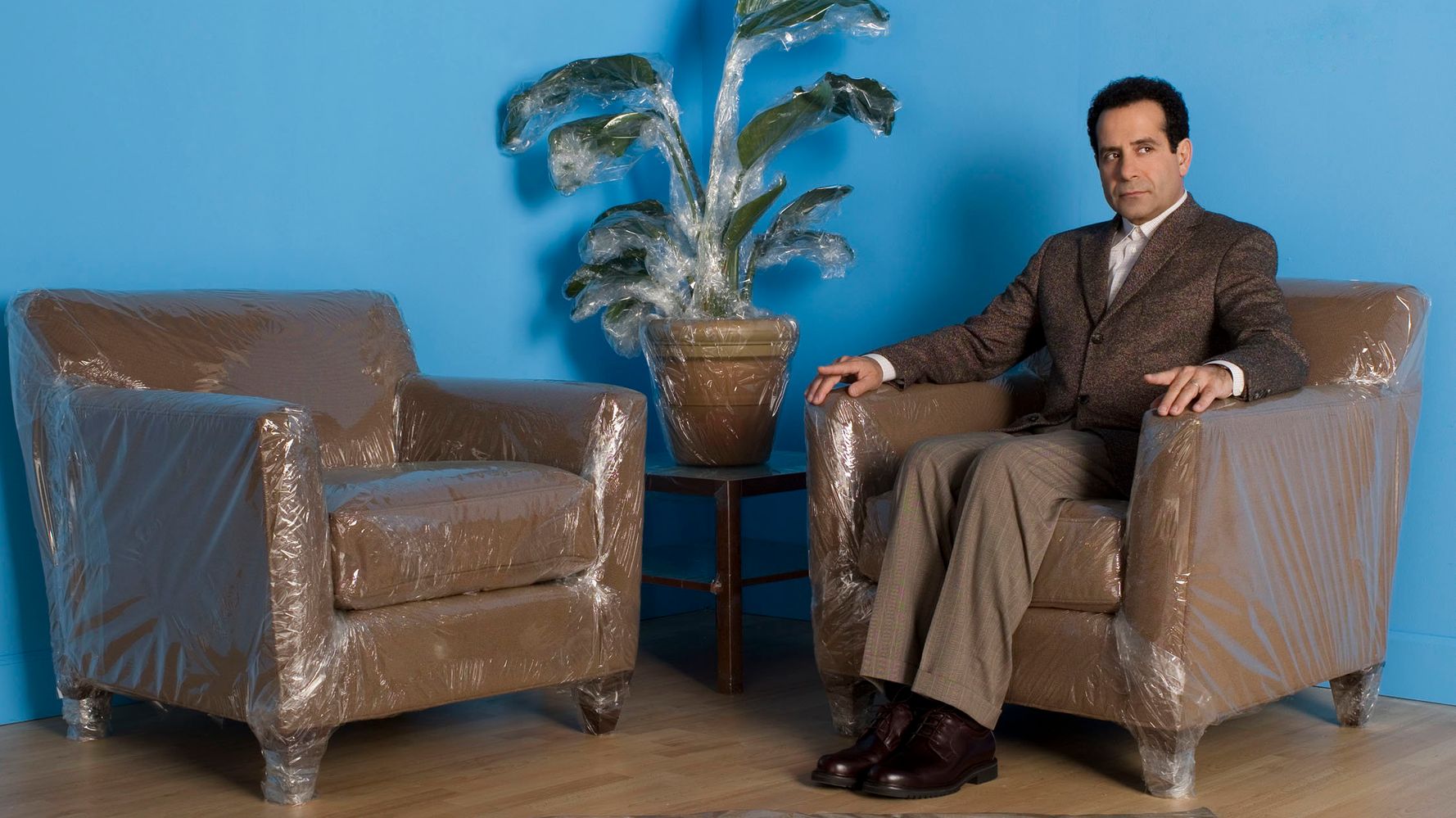 Monk sits on plastic wrapped chairs, safe from germs as he waits alone in a room.