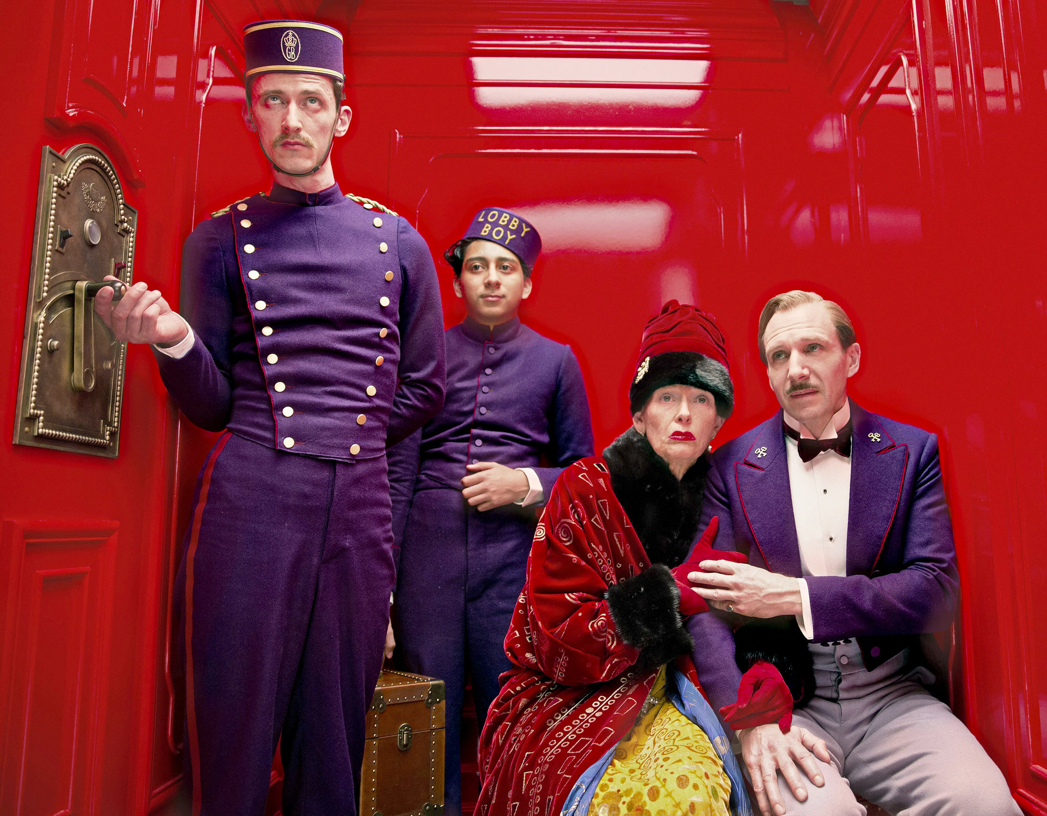 Zero, M. Gustave, Madame D, and the elevator boy stand together in an elevator in The Grand Budapest Hotel