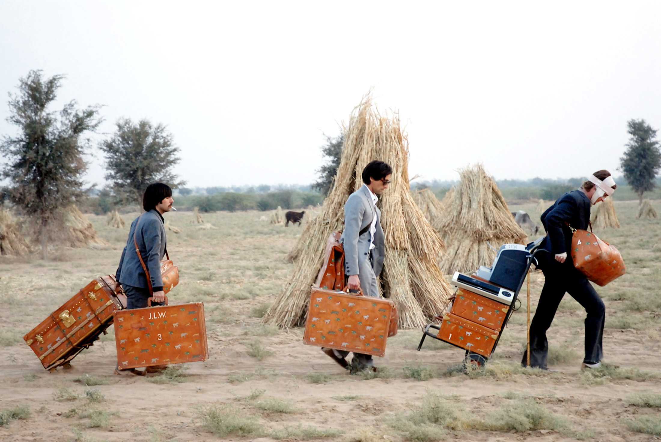 Brothers Peter, Jack, and Francis Whitman walk across a field with their monogrammed luggage in Wes Anderson's film The Darjeeling Limited (2007). 