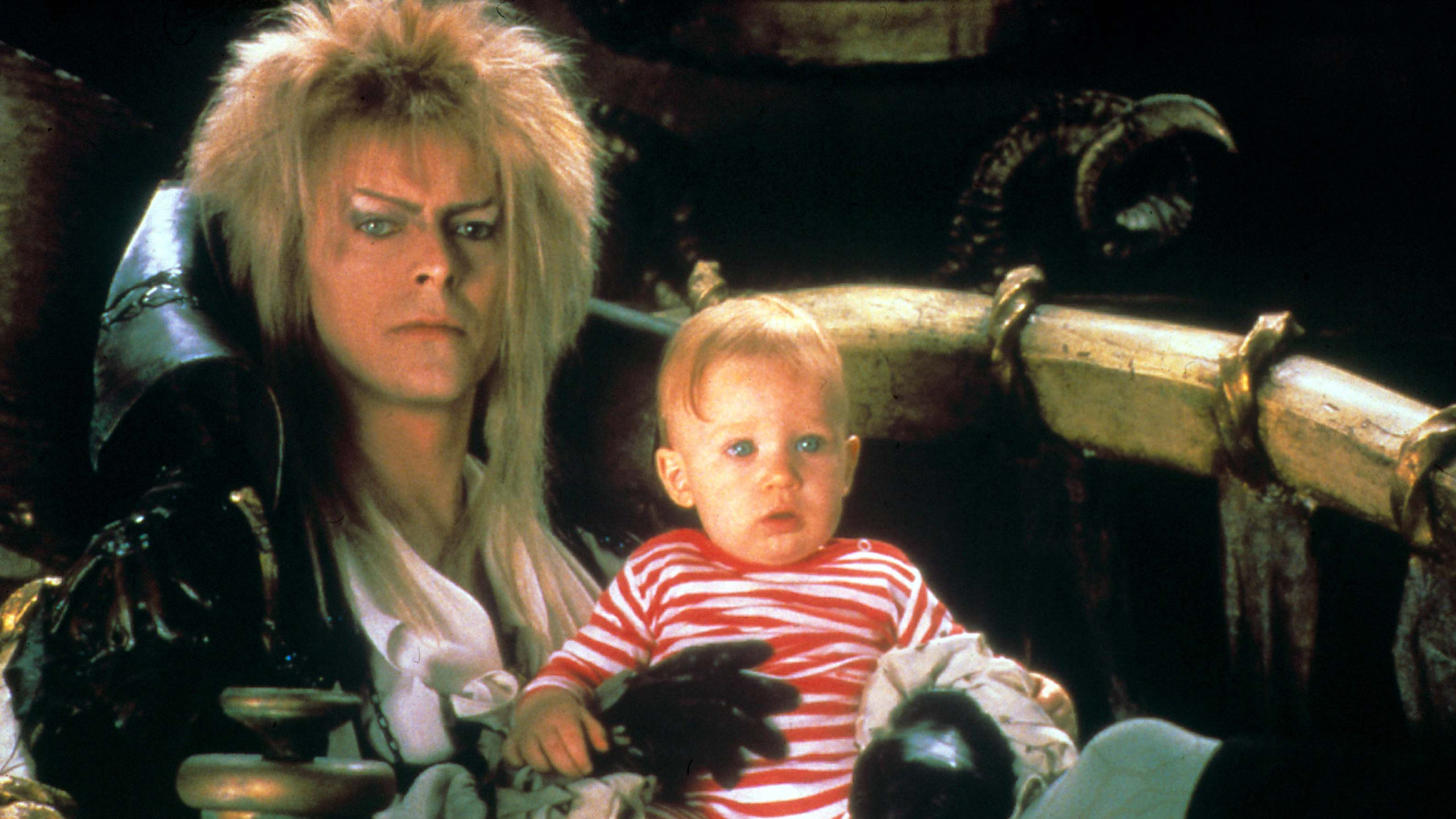 David Bowie, as Jareth, sits with the kidnapped baby. The baby looks totally comfortable.