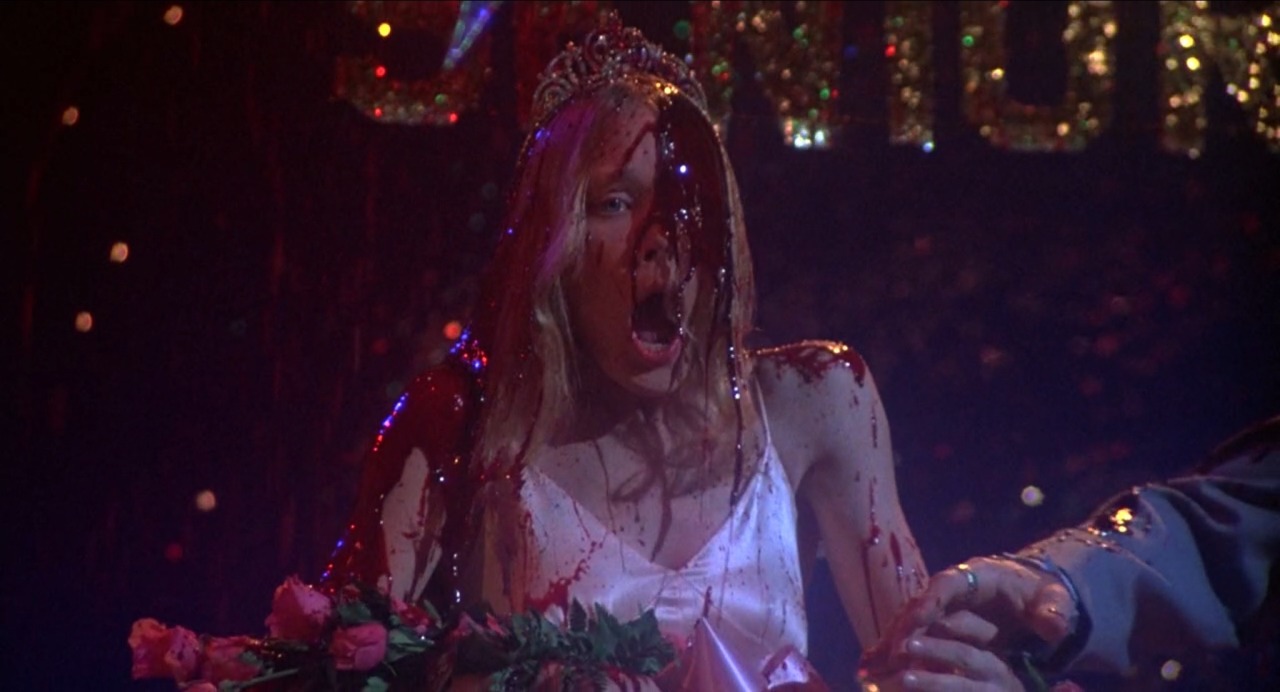 Carrie from the 1976 film, Carrie, stands on stage covered in blood after being crowned prom queen.