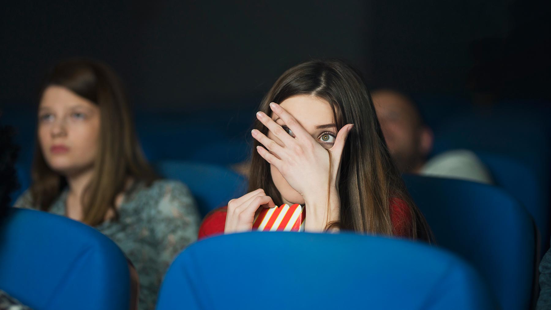 A woman covering her eyes while sitting and watching a horror movie.