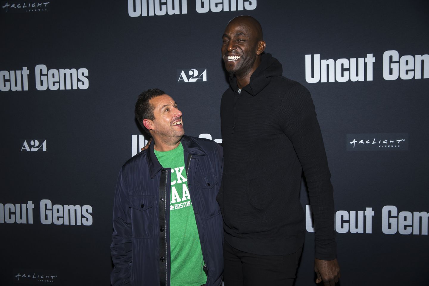 Adam Sandler looks up at Kevin Garnett smiling at a premiere event for Uncut Gems.