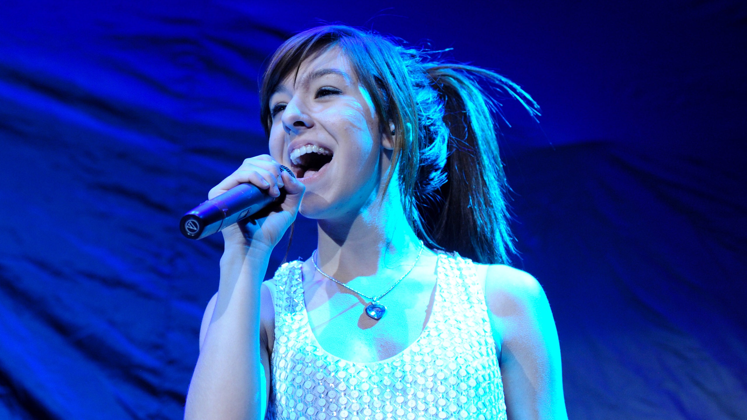 Christina Grimmie singing at a concert with microphone in hand.