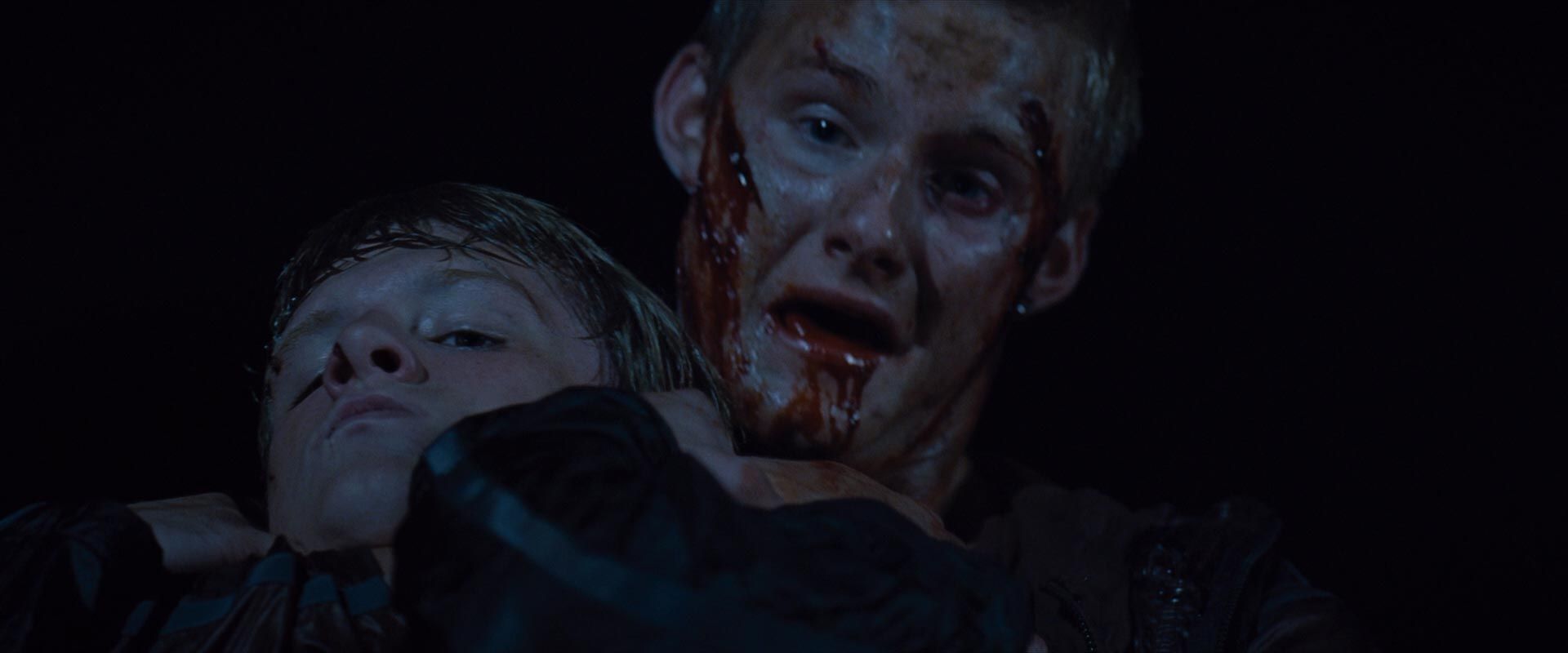 Cato, bloody holds Peeta in a headlock.