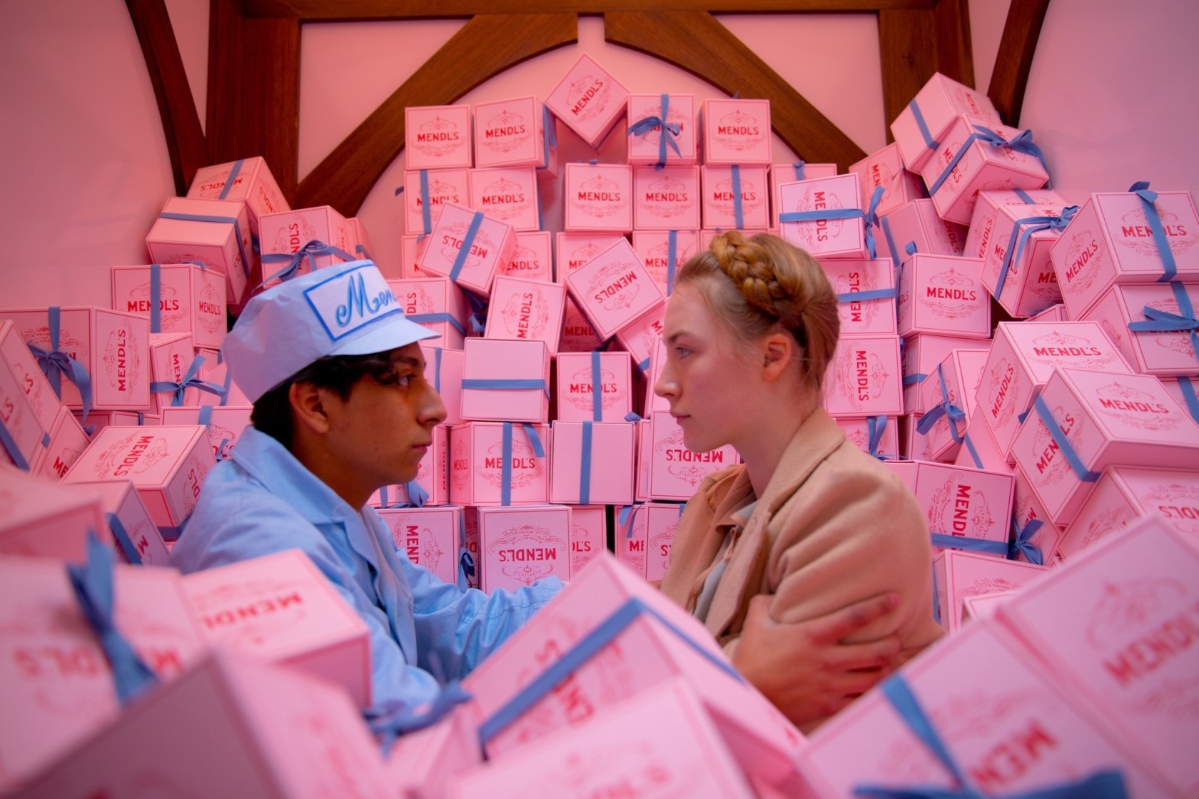 Zero and Agatha from Wes Anderson's movie The Grand Budapest Hotel (2014) hold each other in the back of a truck surrounded by pink pastry boxes. 