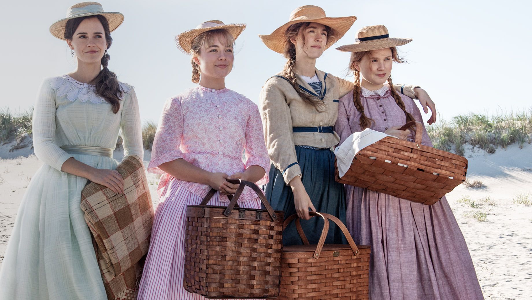 Meg, Jo, Beth, and Amy stand on a beach in dresses, holding baskets.