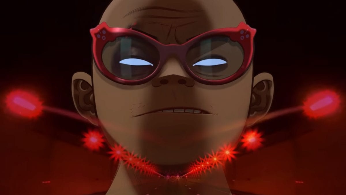 Russel Hobbs frowns in his close-up, wearing red cat glasses in front of a screen showing a dimly-lit road with red light. 