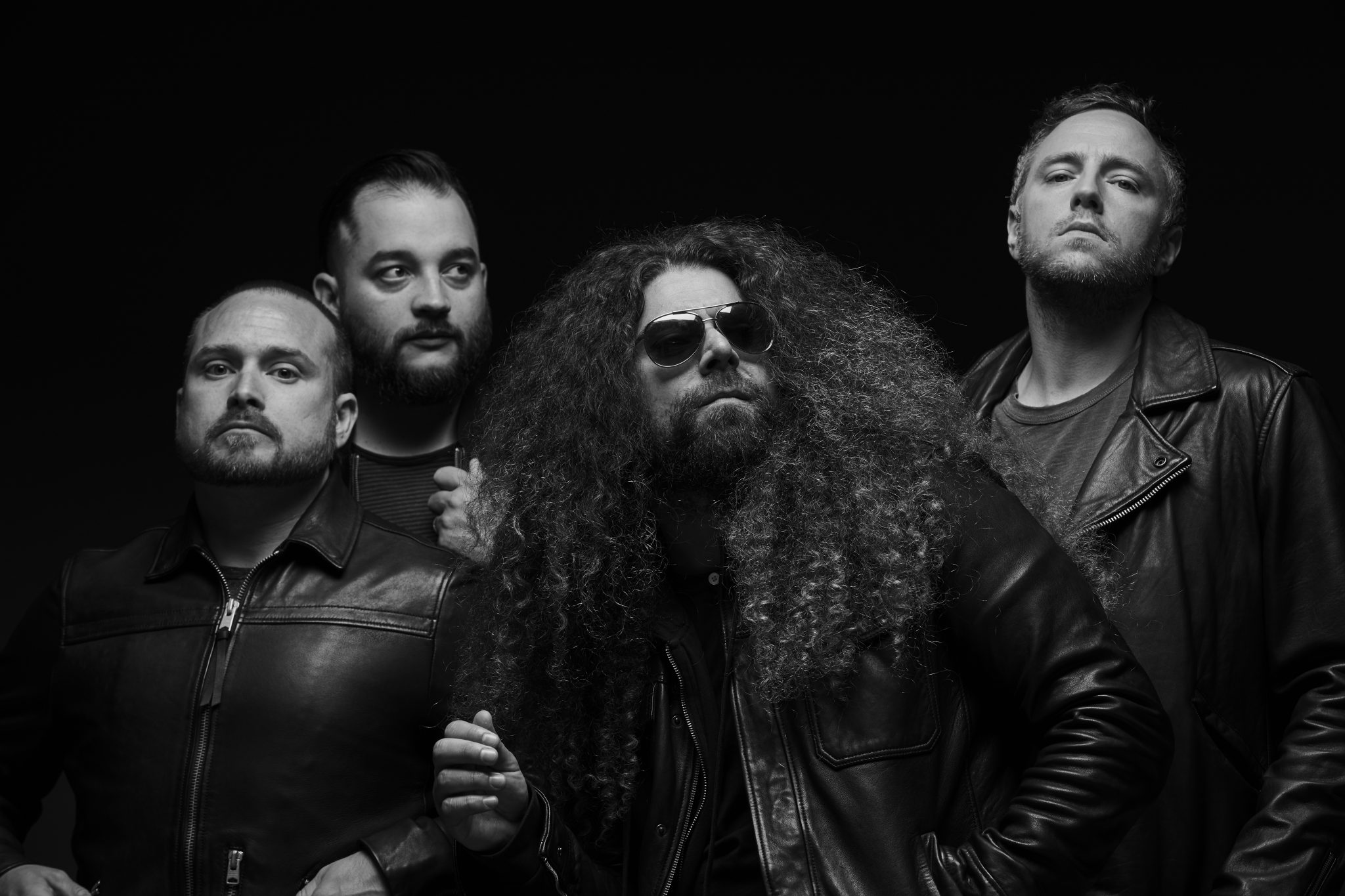 The four band members of Coheed and Cambria pose in front of a black background.